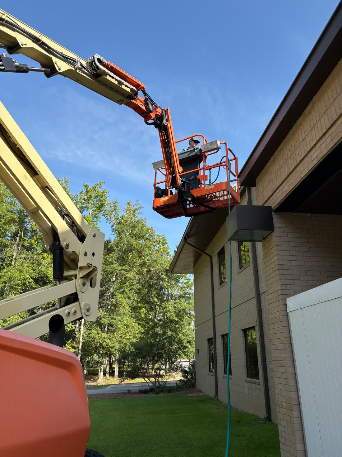Technician working from a boom lift on rooftop HVAC equipment at a two-story commercial building near Statesboro