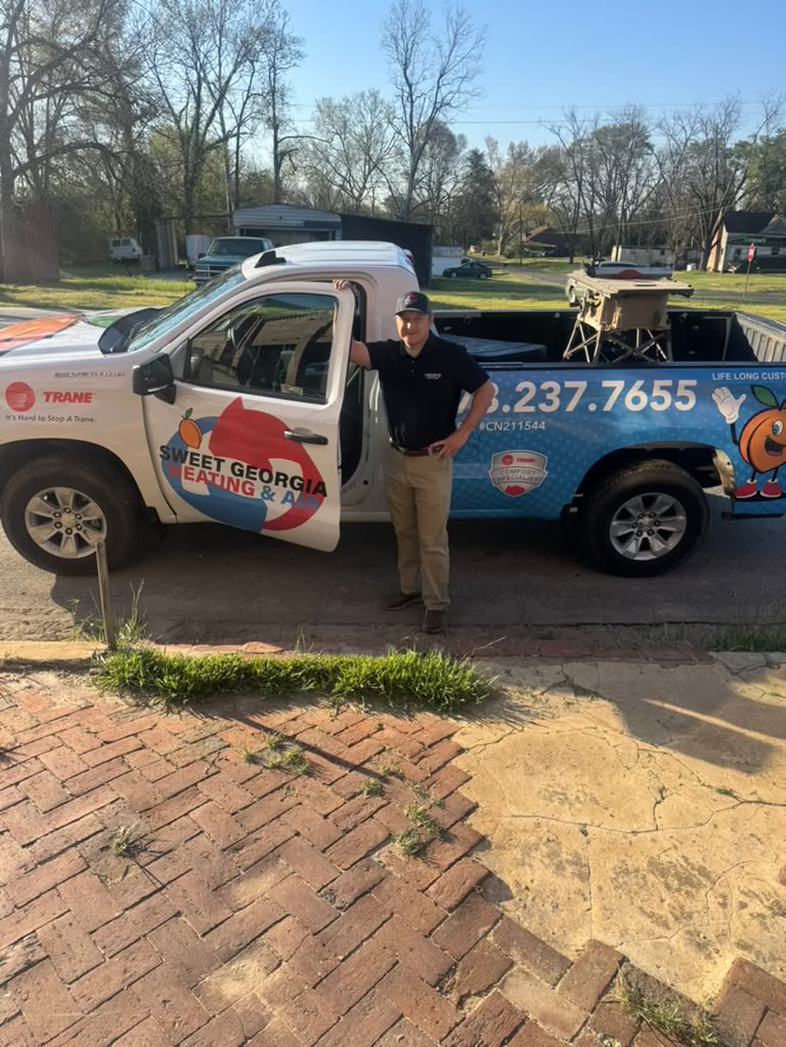 Logan Fuller, owner of Sweet Georgia Heating and Air, beside a company truck on a brick street in Twin City, GA