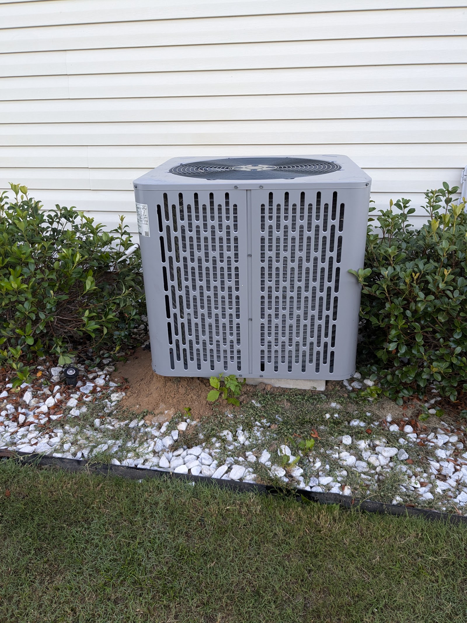 Central air conditioning condenser unit installed beside a home, surrounded by landscaping